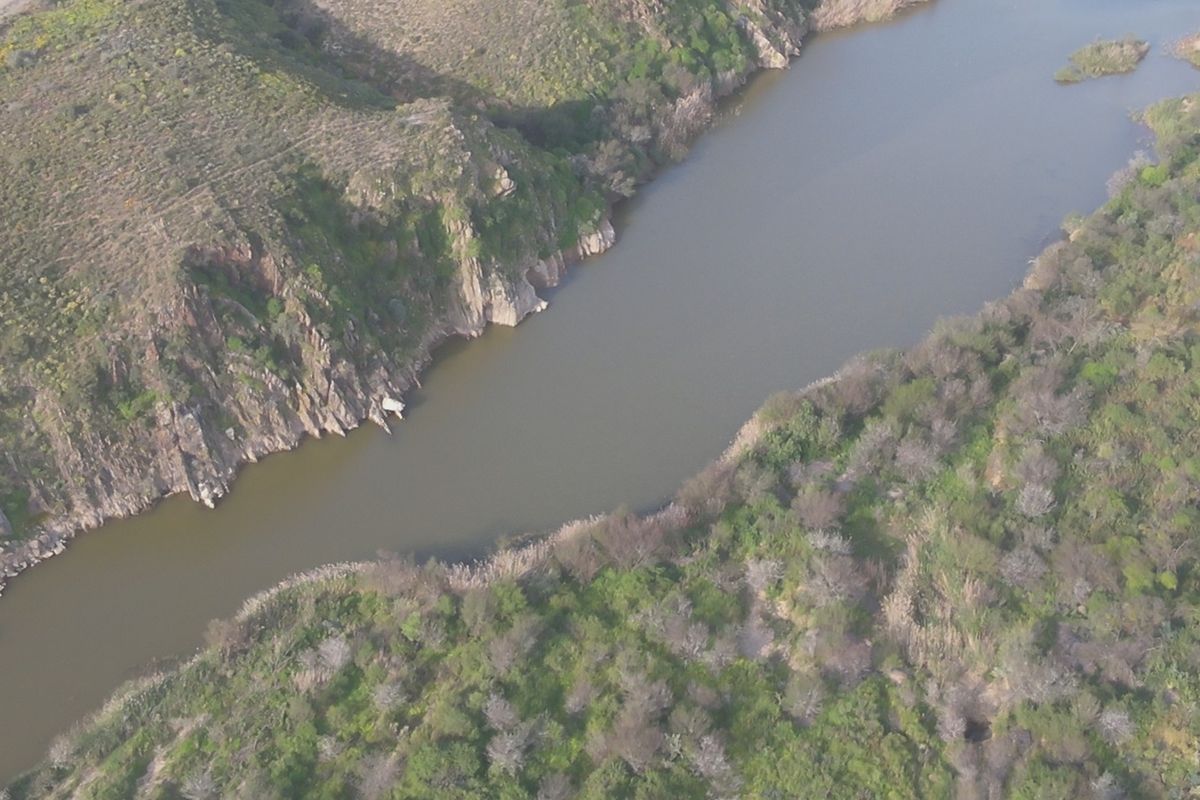 An aerial view of a river flowing through a natural landscape with rocky cliffs and surrounding vegetation.