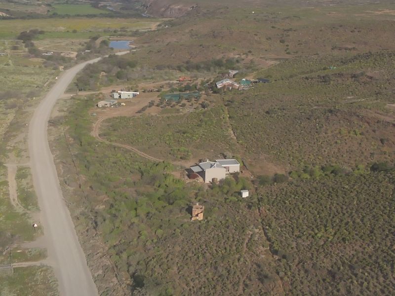 An aerial view of a rural farm property featuring multiple structures, surrounding natural landscape, and access via a gravel road.