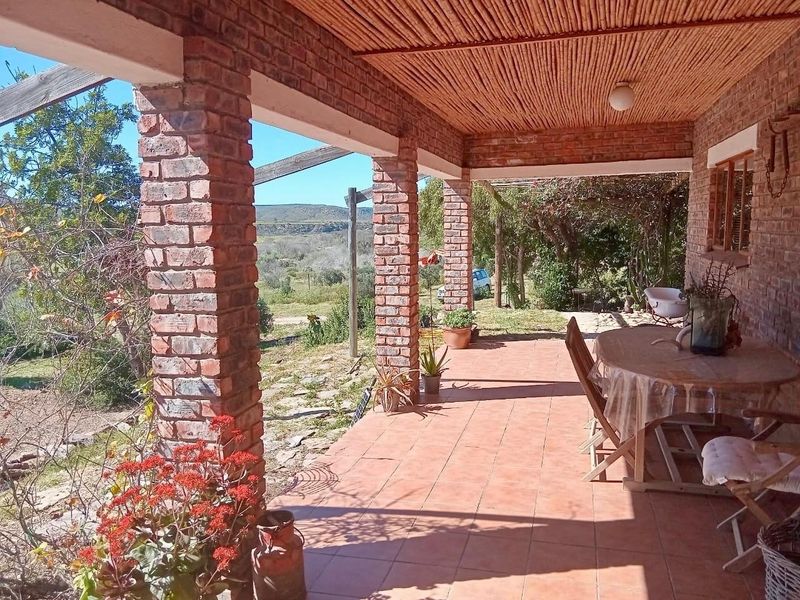 A covered outdoor patio featuring exposed brick columns, a rustic thatched ceiling, and terracotta tiling, offering scenic views of the surrounding farm landscape.