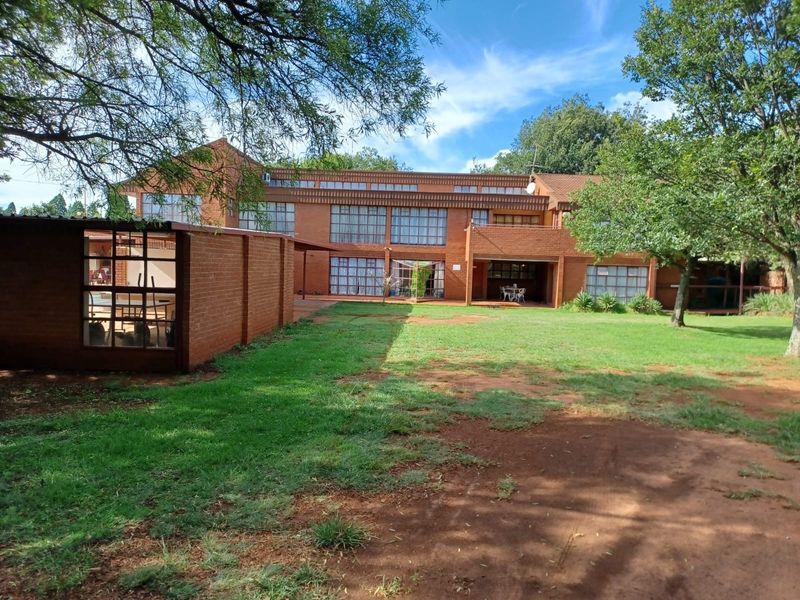 Rear view of a multi-story brick farmhouse featuring large windows, a covered patio area, and a spacious garden with mature trees.