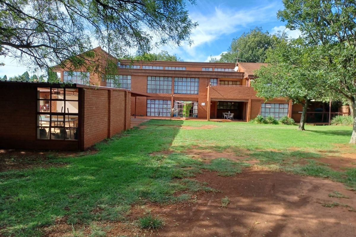 Rear view of a multi-story brick farmhouse featuring large windows, a covered patio area, and a spacious garden with mature trees.