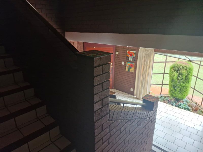 An entrance area featuring a brick staircase, tiled flooring, and a large window overlooking the garden, providing a rustic and solid architectural aesthetic.