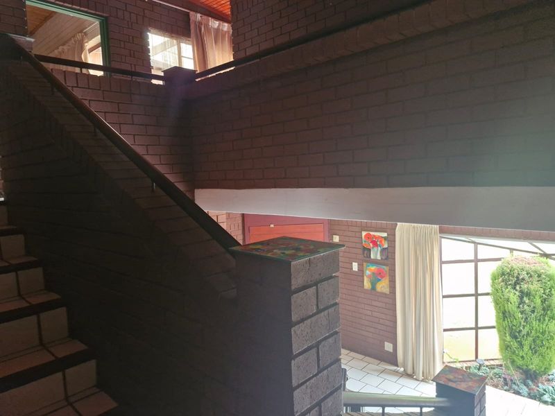 A spacious interior hallway featuring exposed brick walls, a brick staircase with a balustrade, and large windows providing natural light.