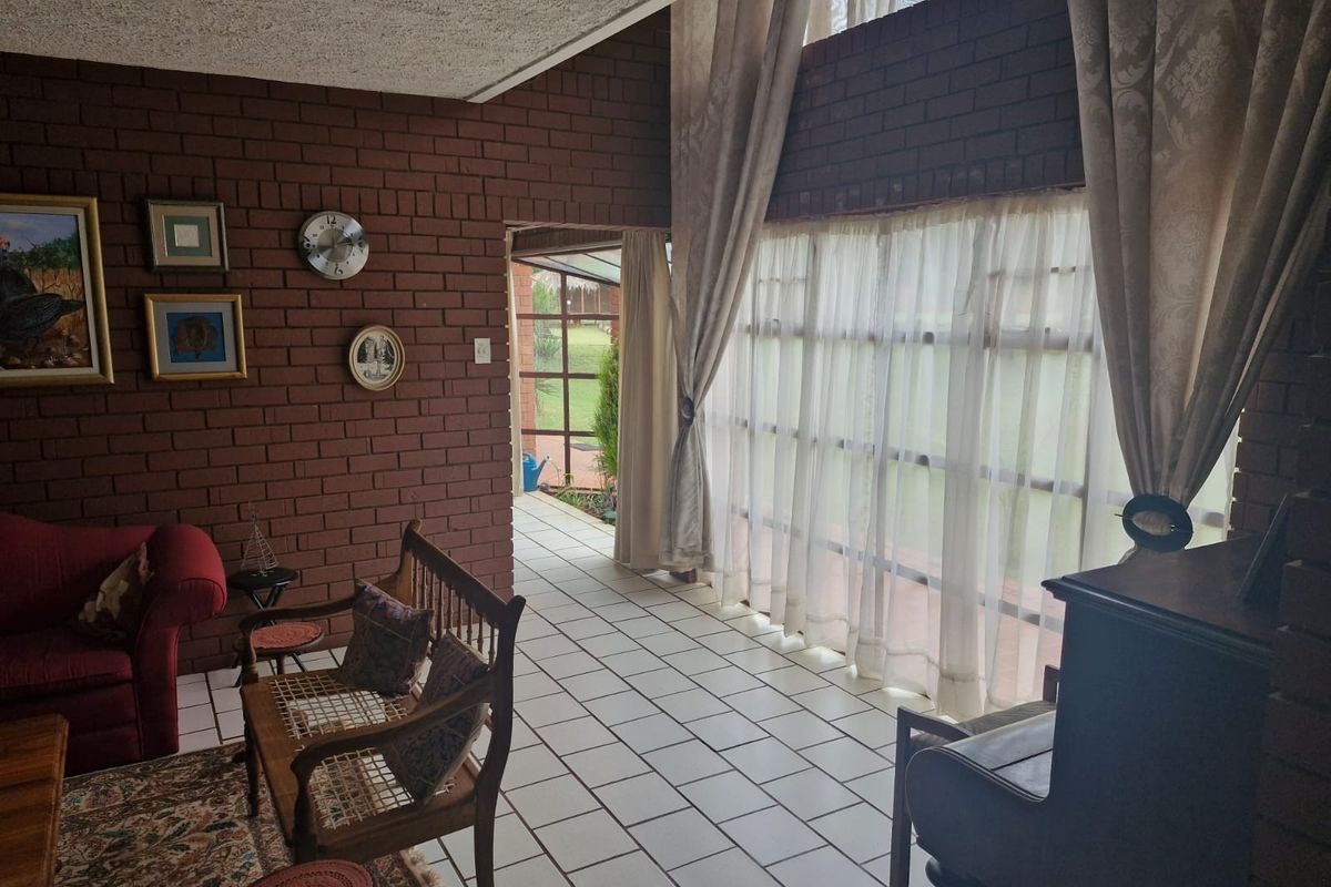 Spacious living area featuring exposed brick walls, double volume ceilings, and large windows that provide ample natural light and access to the patio.