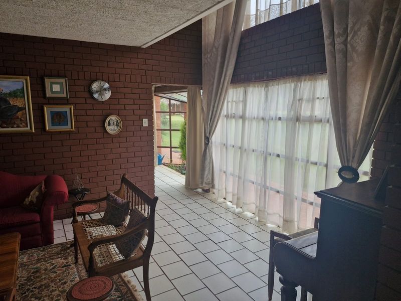 Spacious living area featuring exposed brick walls, double volume ceilings, and large windows that provide ample natural light and access to the patio.