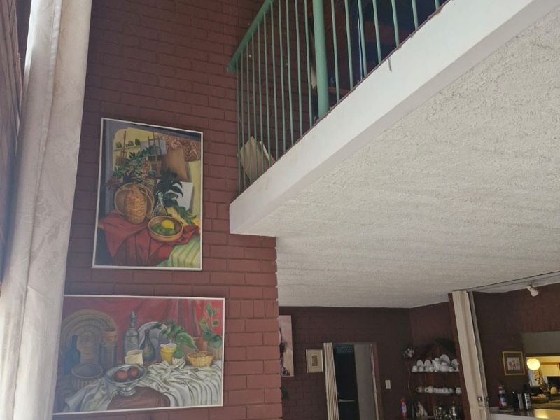 Spacious living area featuring double-volume ceilings, exposed brickwork, and a mezzanine level with a metal balustrade, offering a unique architectural layout.