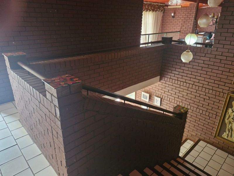 A spacious interior hallway featuring a distinctive brick staircase and balustrade with tiled flooring and pendant lighting.
