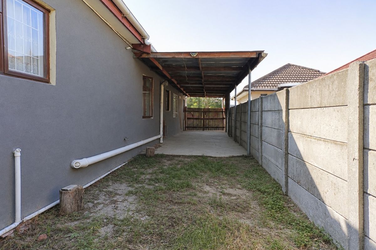 Side exterior area featuring a concrete driveway, a covered carport structure, and a precast concrete boundary wall with a timber gate.