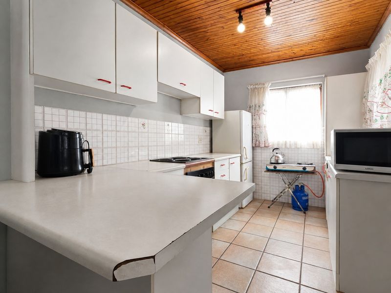 A dated kitchen featuring white cabinetry, tiled backsplash, laminate countertops, and a timber ceiling, offering potential for a modern renovation.