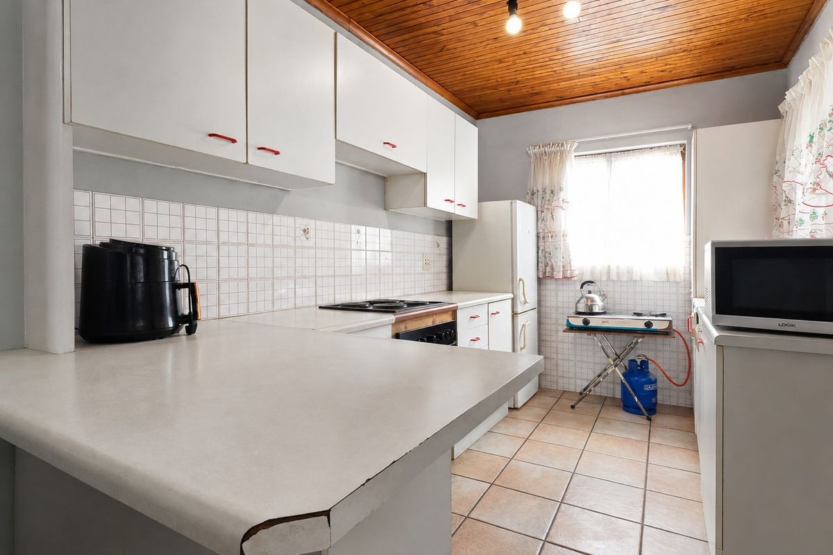 A dated kitchen featuring white cabinetry, tiled backsplash, laminate countertops, and a timber ceiling, offering potential for a modern renovation.