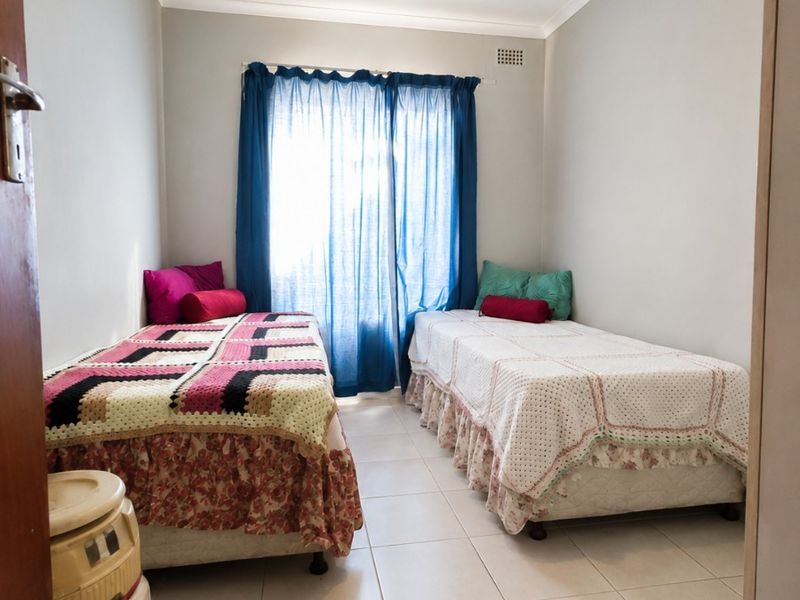 A functional bedroom featuring neutral tiled flooring, simple cove cornicing, and a central pendant light fixture with natural light from the window.
