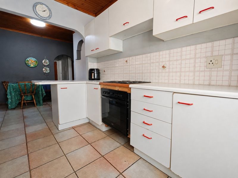 A functional kitchen featuring white cabinetry, a built-in oven and hob, tiled backsplash, and terracotta-style floor tiles with a timber ceiling.