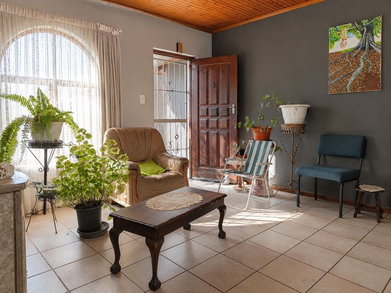A living room featuring tiled flooring, a timber ceiling, and an arched window, providing access to the exterior through a timber door.