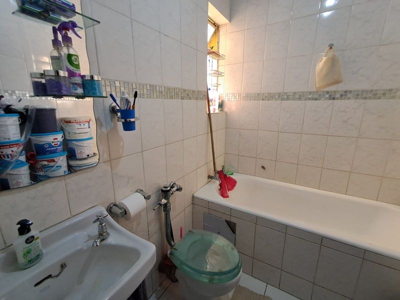 A functional bathroom featuring a bathtub, toilet, and washbasin with tiled walls and flooring. The space requires minor maintenance and cosmetic updates.