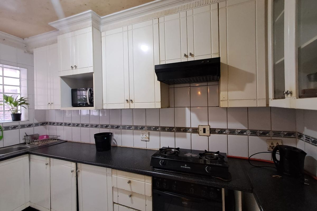 A functional kitchen featuring white cabinetry, dark countertops, a gas hob, and a tiled backsplash, requiring cosmetic updates to modernize the space.