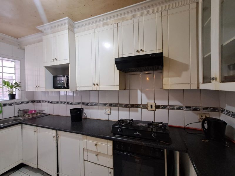 A functional kitchen featuring white cabinetry, dark countertops, a gas hob, and a tiled backsplash, requiring cosmetic updates to modernize the space.