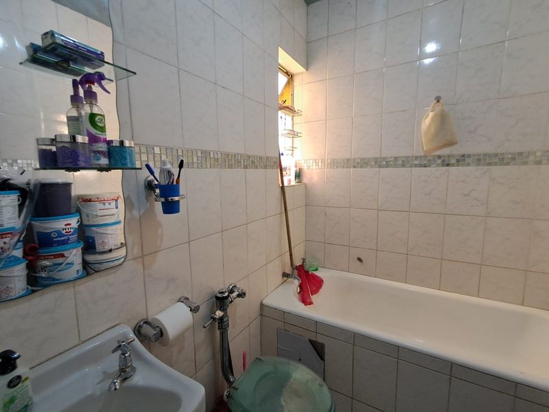 A compact bathroom featuring a bathtub, wall-mounted basin, and tiled walls with a mosaic accent border, requiring some maintenance and cosmetic updates.
