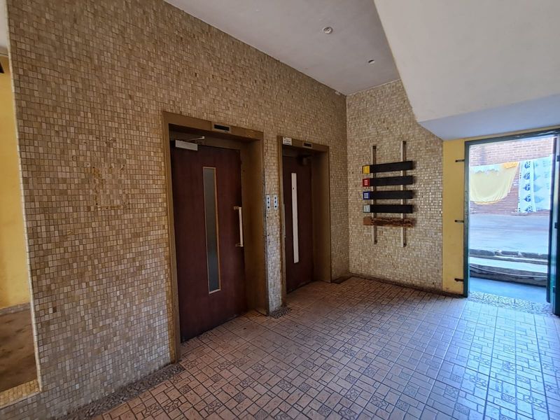 Apartment building lobby area featuring dual elevators, mosaic wall tiling, and ceramic floor tiles, providing access to the exterior entrance.