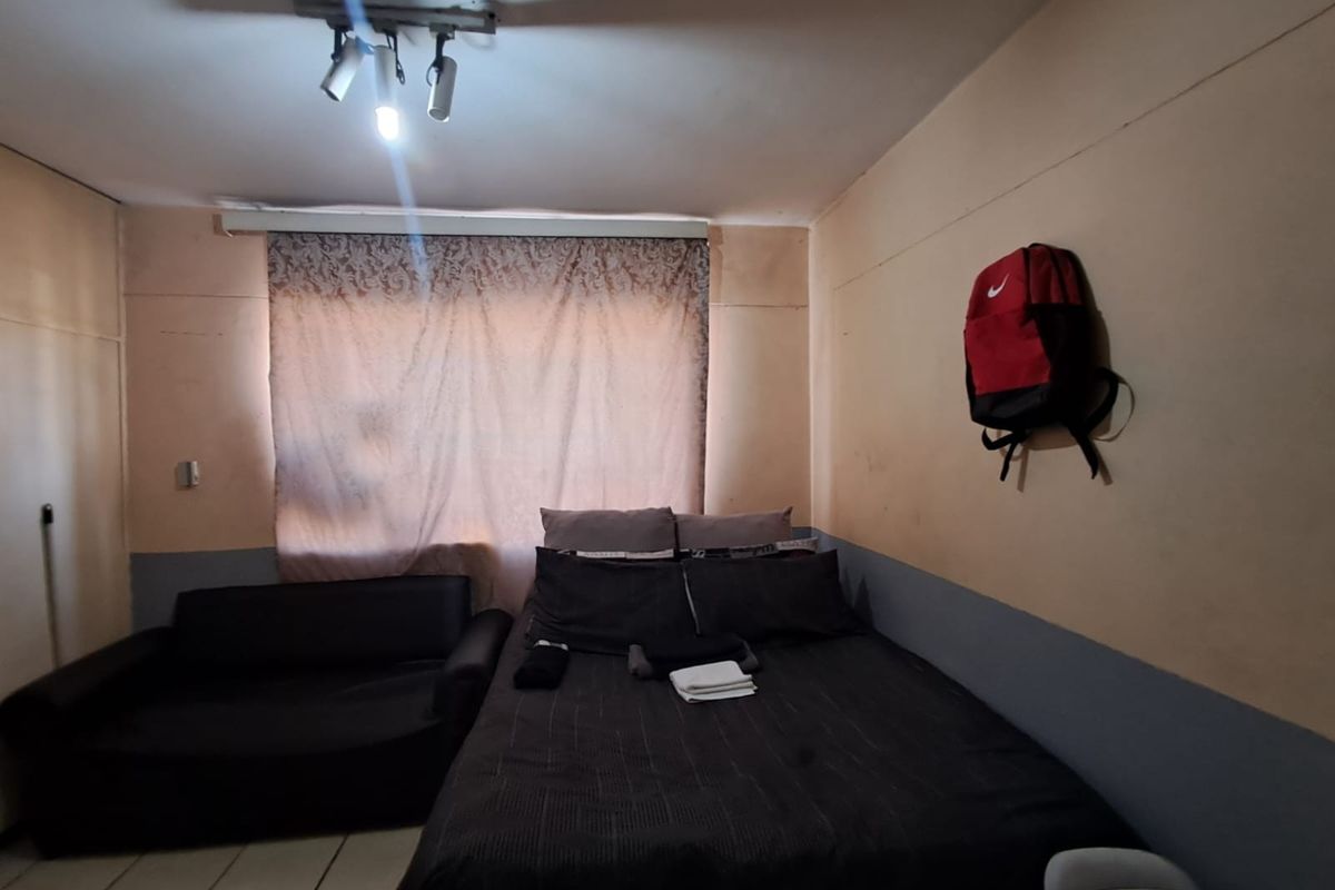 A bedroom featuring tiled flooring and track lighting, currently showing signs of wear on the wall surfaces.