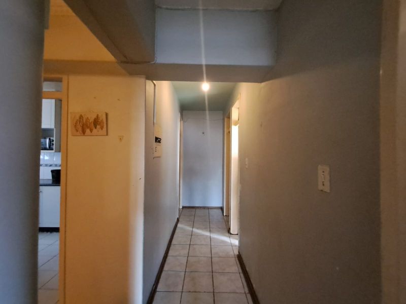 A functional hallway featuring tiled flooring and access to adjacent rooms, showing signs of wear on the walls.