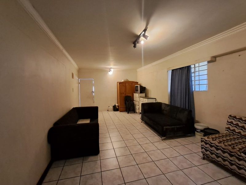 A spacious living area featuring tiled flooring, track lighting, and decorative cornice, offering a blank canvas for potential interior updates.