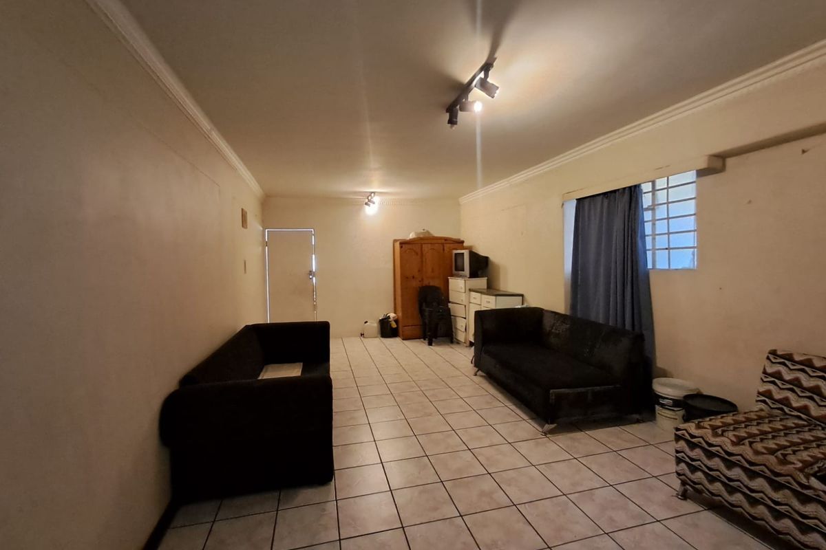 A spacious living area featuring tiled flooring, track lighting, and decorative cornice, offering a blank canvas for potential interior updates.