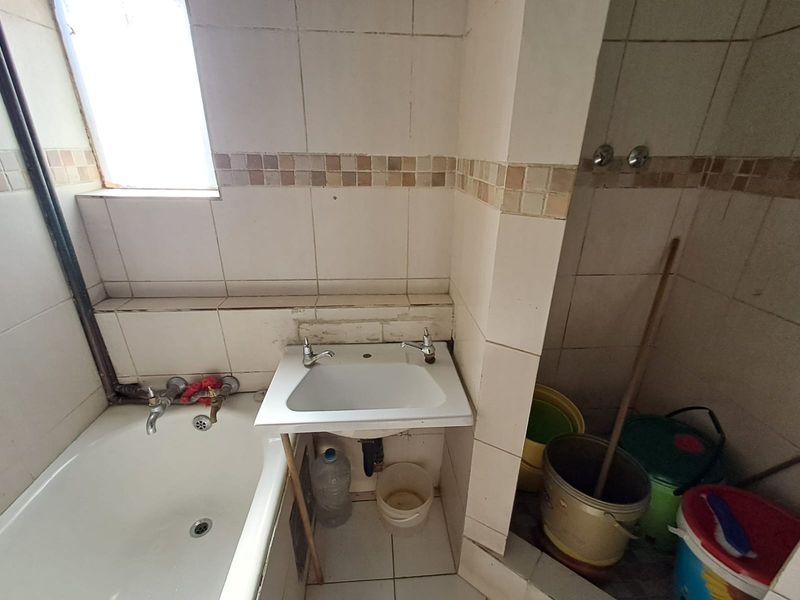 A dated bathroom featuring a bathtub and wall-mounted basin with visible tile damage and exposed plumbing, requiring renovation to improve functionality and aesthetic appeal.