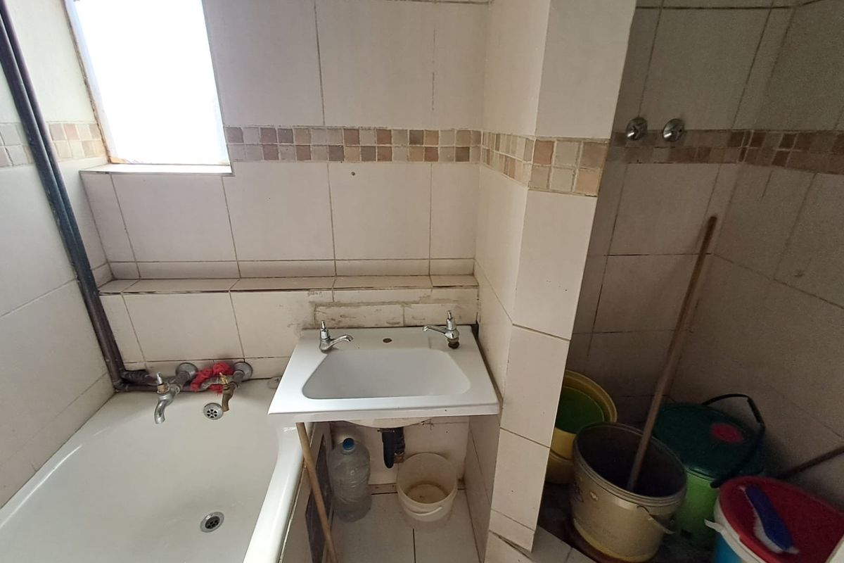 A dated bathroom featuring a bathtub and wall-mounted basin with visible tile damage and exposed plumbing, requiring renovation to improve functionality and aesthetic appeal.