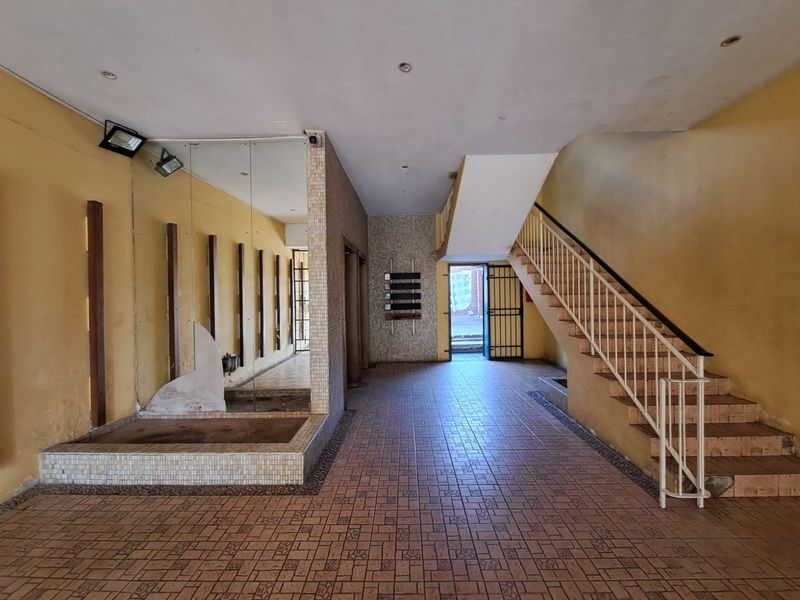 Spacious apartment building entrance lobby featuring tiled flooring, a staircase with metal balustrade, and decorative mosaic wall elements.