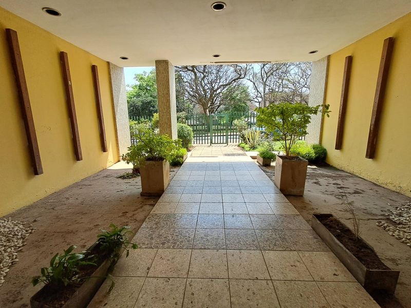 Covered entrance walkway featuring tiled flooring, recessed lighting, and built-in concrete planters leading to a secure metal gate.