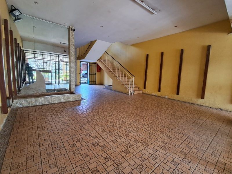 Spacious entrance hall featuring tiled flooring, a central staircase, and security gate access, presenting a dated interior in need of cosmetic refurbishment.