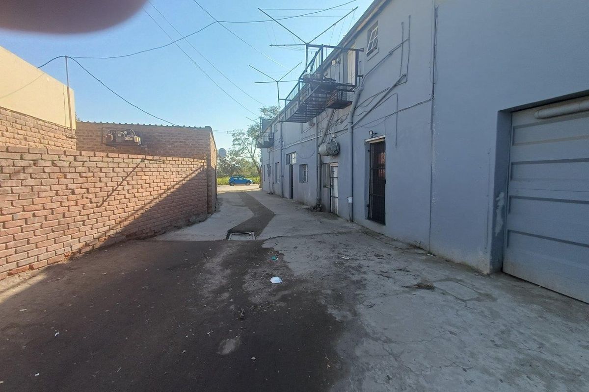 Rear exterior view of a commercial building featuring a concrete driveway, brick boundary wall, and external metal fire escape access.