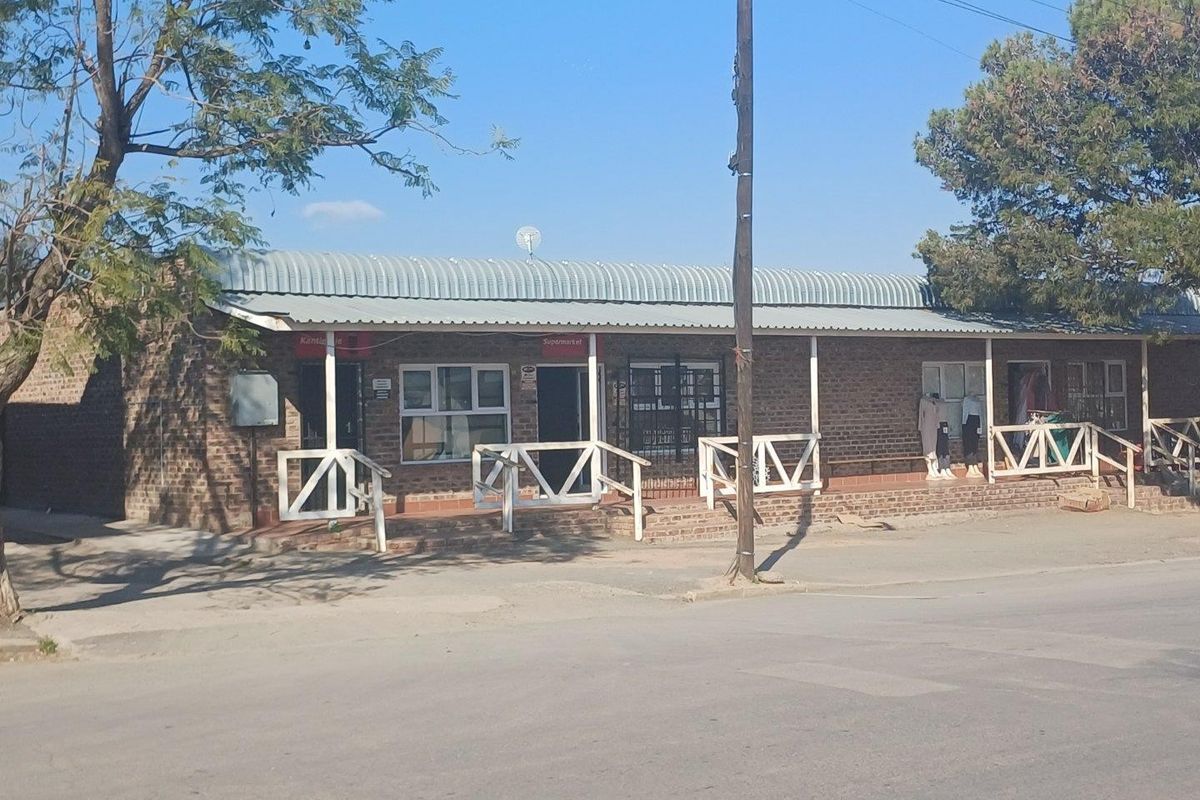 Single-story commercial building featuring a brick facade, corrugated metal roof, and a covered veranda with timber railings.