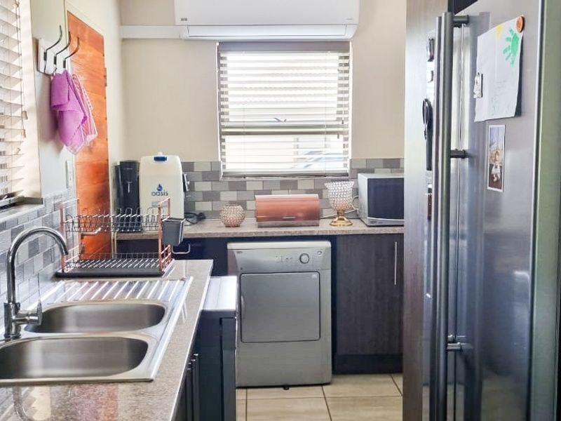 A functional scullery featuring double bowl sink, tiled splashbacks, ample cabinetry, and a wall-mounted air conditioning unit.