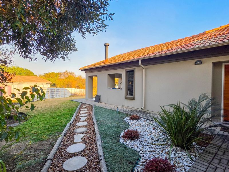 A well-maintained rear exterior view featuring a terracotta tiled roof, a paved garden path, and a landscaped yard with a timber entrance door.
