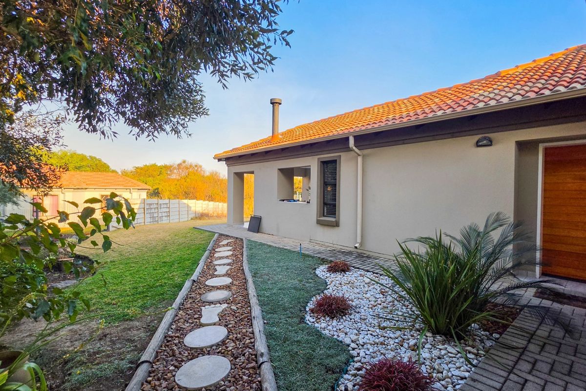 A well-maintained rear exterior view featuring a terracotta tiled roof, a paved garden path, and a landscaped yard with a timber entrance door.