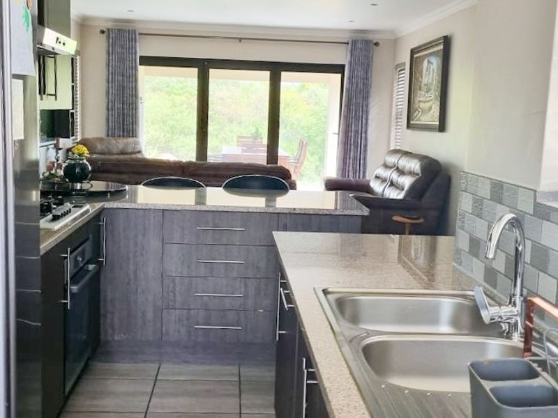Open-plan kitchen featuring granite countertops, built-in oven, gas hob, and double sink, flowing seamlessly into the adjacent living area with garden access.