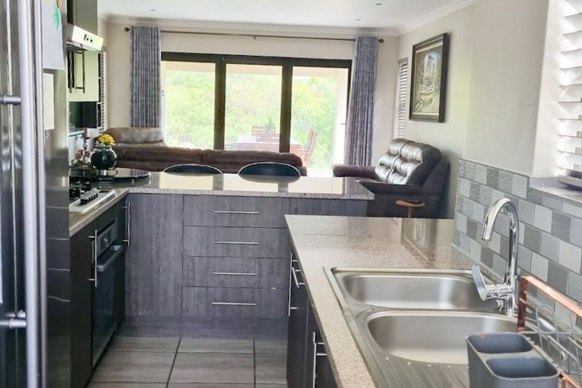 Open-plan kitchen featuring granite countertops, built-in oven, gas hob, and double sink, flowing seamlessly into the adjacent living area with garden access.