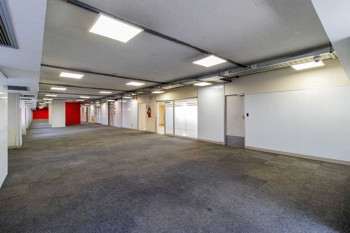 A spacious, open-plan commercial office area featuring carpeted flooring, recessed LED lighting, exposed cable management systems, and glass-partitioned office suites.