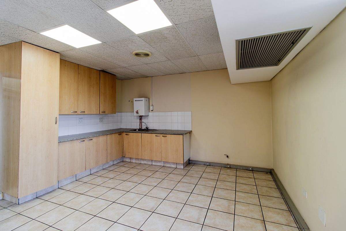 A functional commercial kitchenette featuring laminate cabinetry, granite countertops, tiled flooring, and a drop ceiling with integrated lighting.