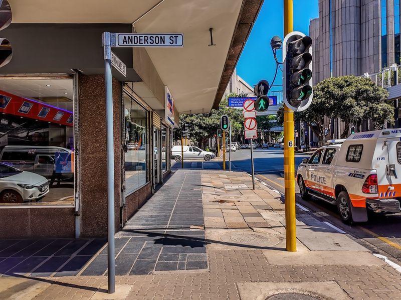 Street-level view of a commercial property corner at the intersection of Anderson and Simmonds Street, featuring storefront glazing and public sidewalk access.