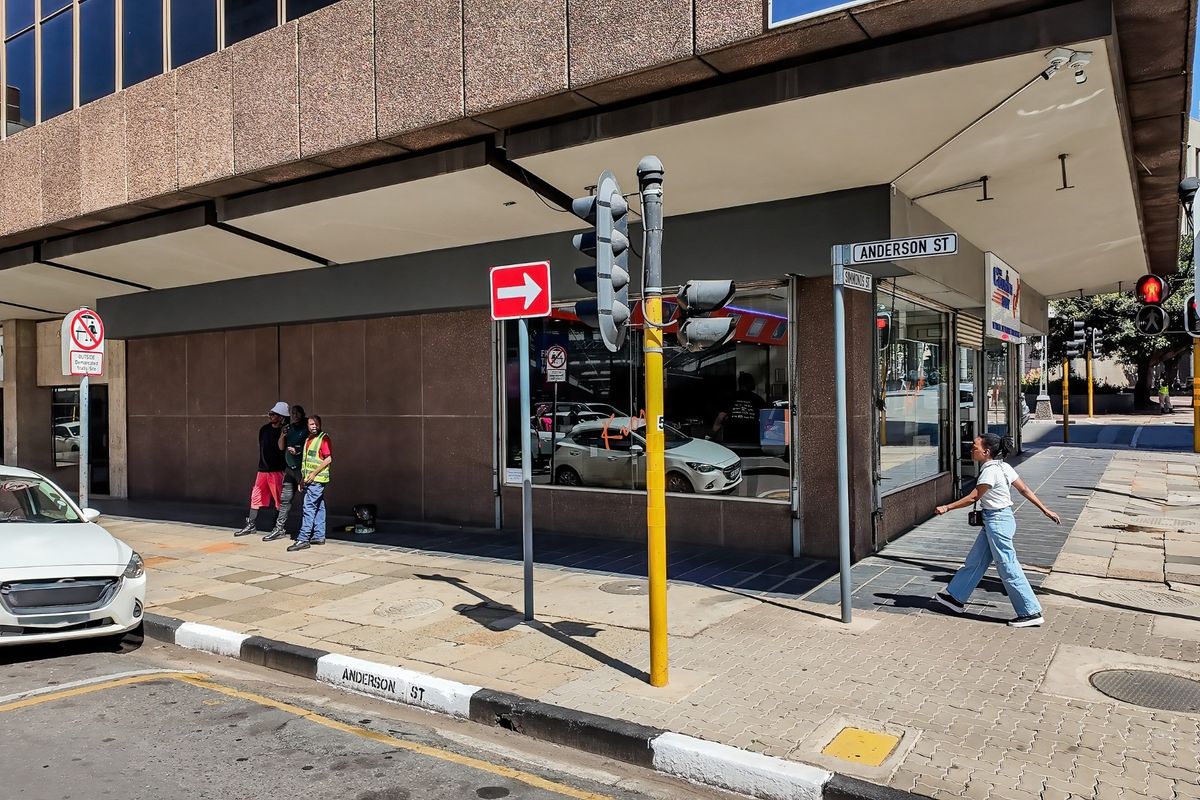 Street-level view of a commercial building corner featuring large display windows, paved sidewalk access, and prominent street signage at the intersection.