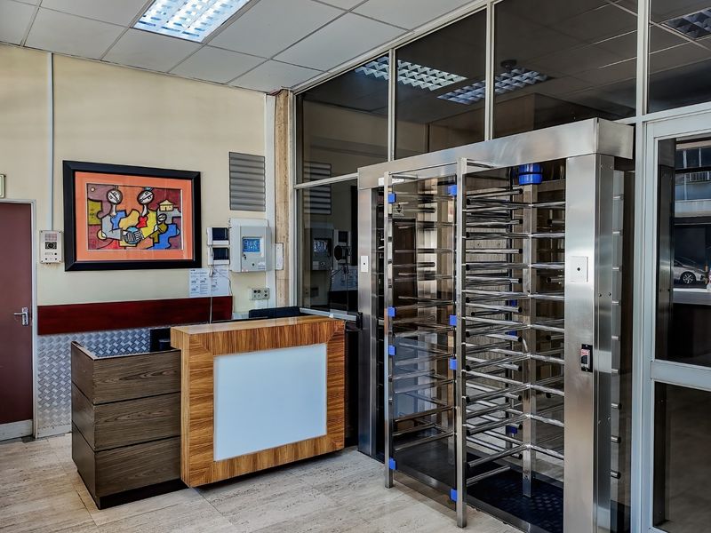 Commercial building entrance featuring a security turnstile, reception desk, and tiled flooring with professional lighting and aluminium framed glass partitions.