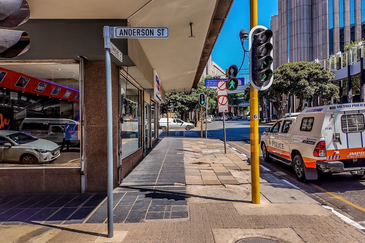 Street-level view of a commercial property corner at the intersection of Anderson and Simmonds Street, featuring storefront glazing and public sidewalk access.