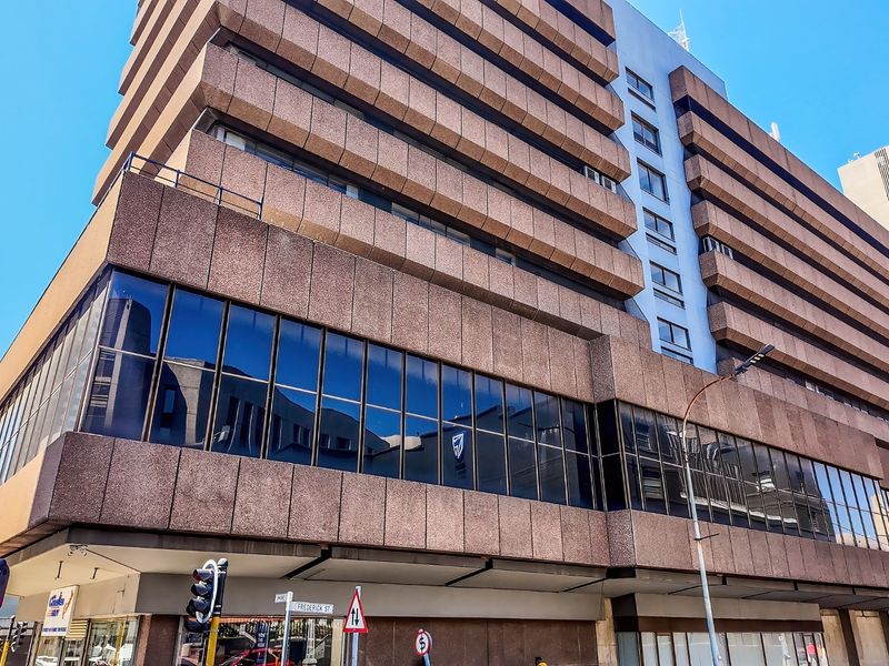A multi-story commercial office building featuring a prominent concrete facade and extensive street-level glass curtain walling on a corner plot.