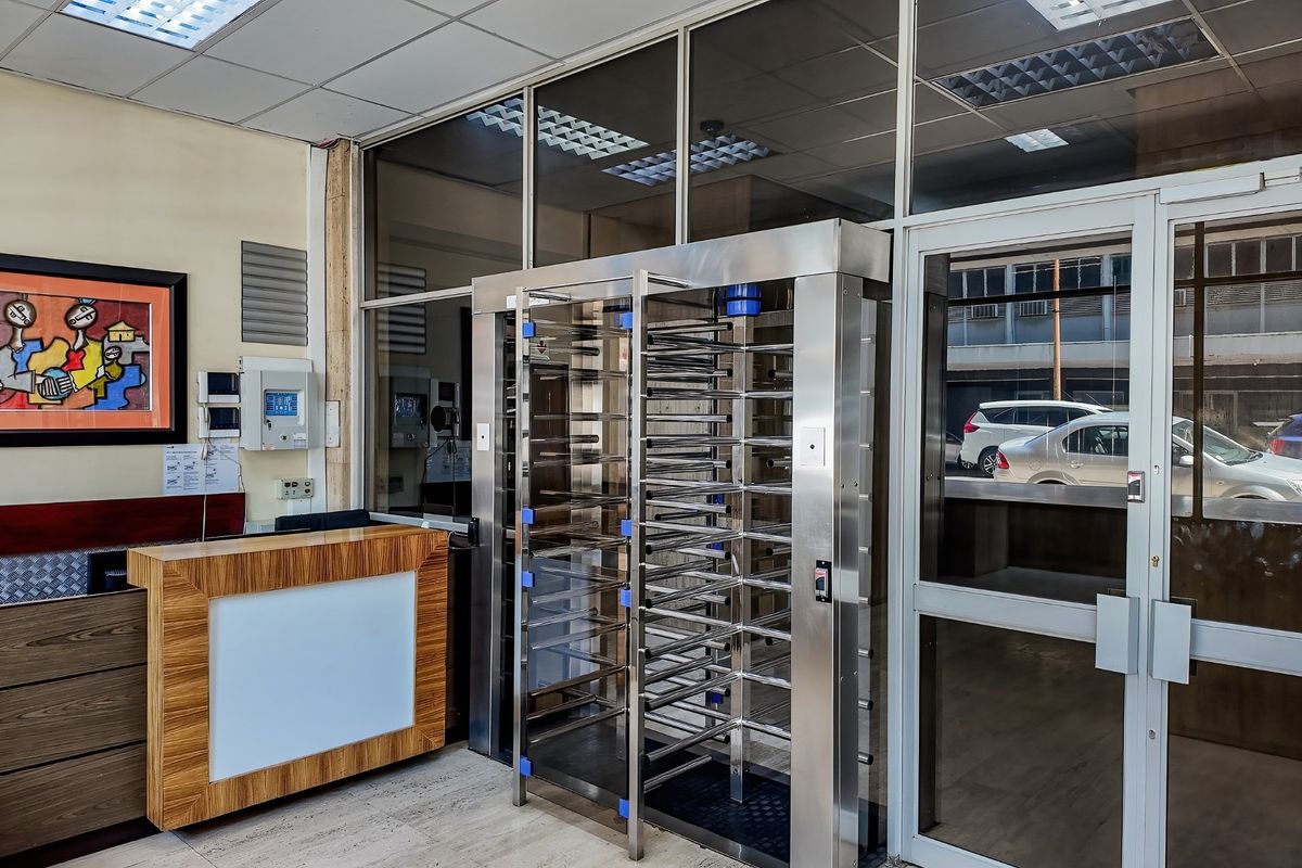 Commercial building entrance featuring a stainless steel security turnstile, reception desk, and glass partition wall with integrated security systems.