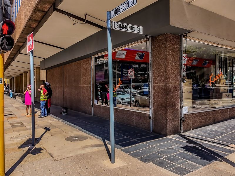 Street-level view of a commercial property corner featuring large display windows, a covered walkway, and prominent street signage at the intersection.