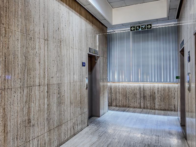 A professional commercial elevator lobby featuring high-quality travertine wall and floor finishes, integrated elevator access, and modern emergency signage.