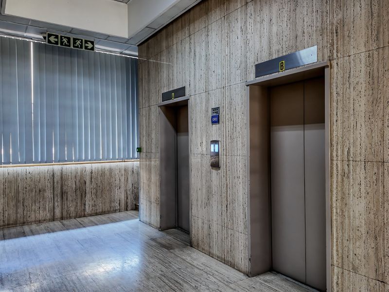 Commercial elevator lobby featuring travertine wall cladding, stone flooring, and integrated elevator access points.