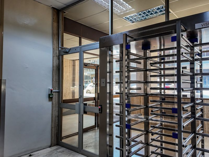 Commercial building entrance lobby featuring a stainless steel visitor turnstile, glass security doors, and stone flooring.